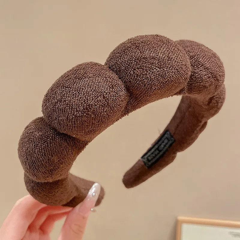 A close-up of a brown, textured sponge hair accessory headband being held by a hand.