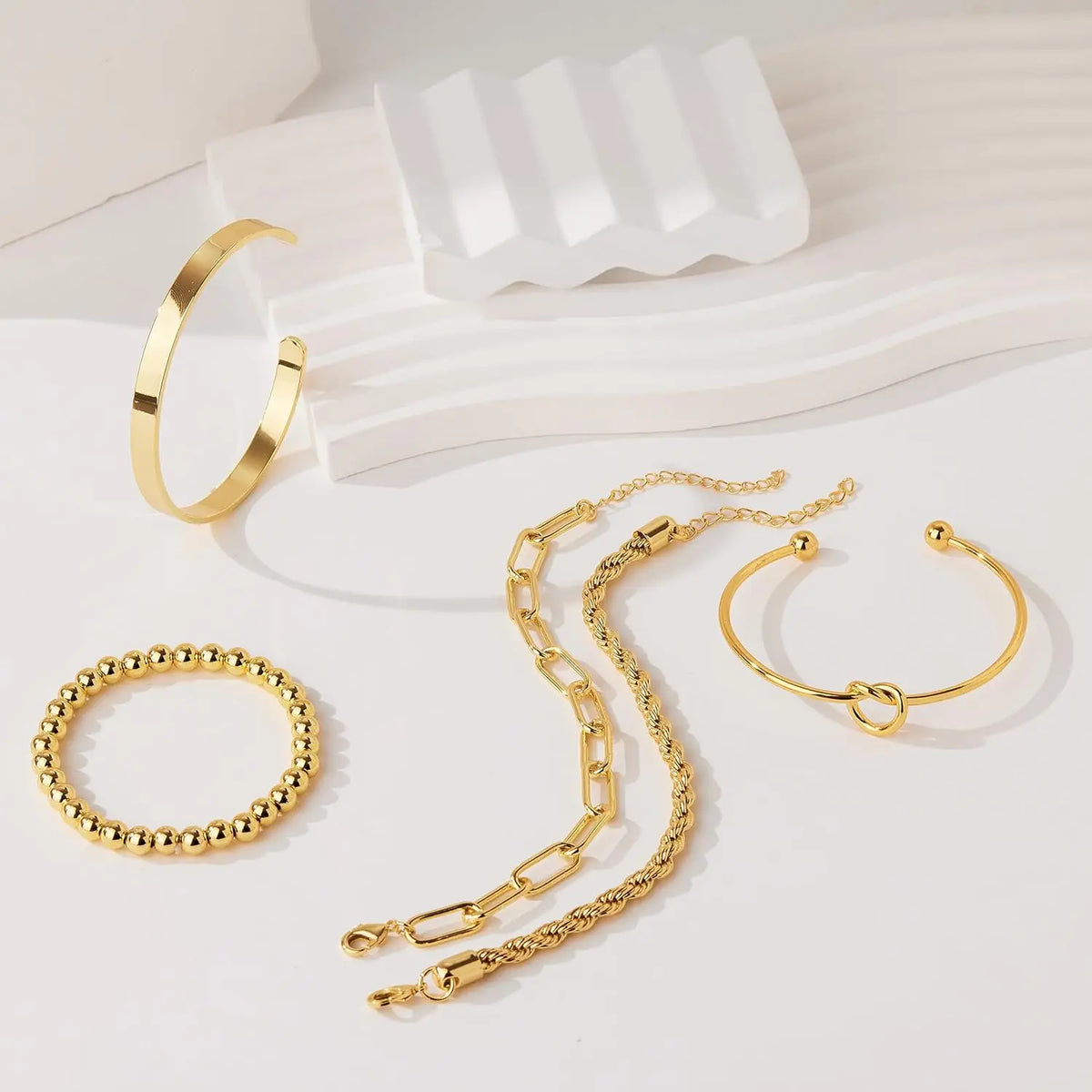 A collection of 14K gold plated chunky cuff bangles and a simple gold chain bracelet displayed on a white background.
