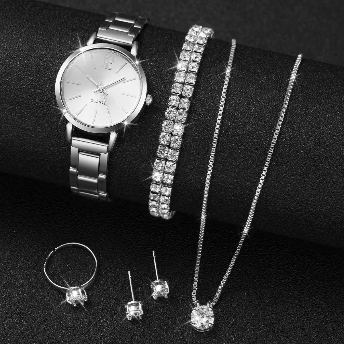 A silver quartz wristwatch, a diamond bracelet, and several diamond necklaces displayed on a black surface.