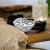 A silver fashion quartz wristwatch with a Roman dial and black leather strap resting on a wooden surface.