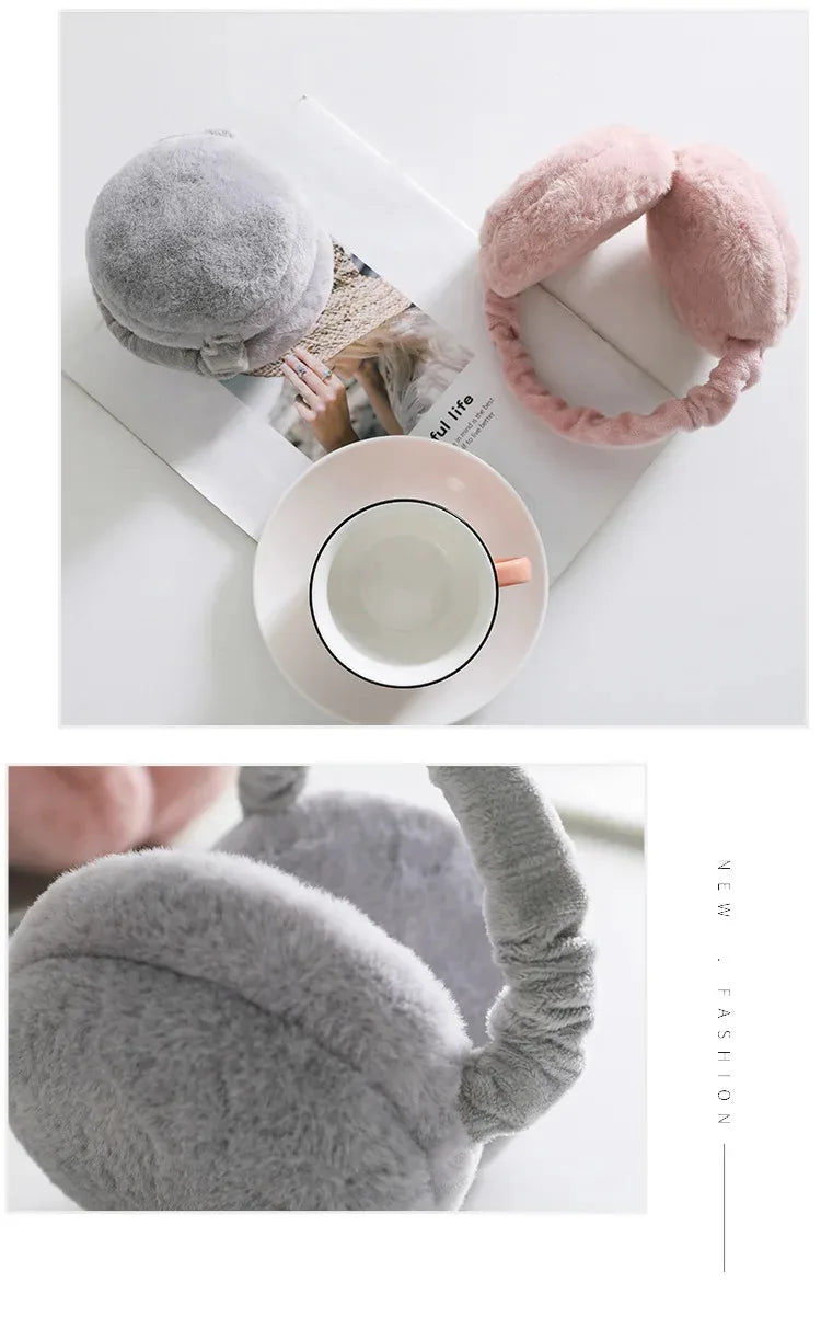 A pair of pink plush fur ear muffs resting on a white surface next to a cup and saucer.