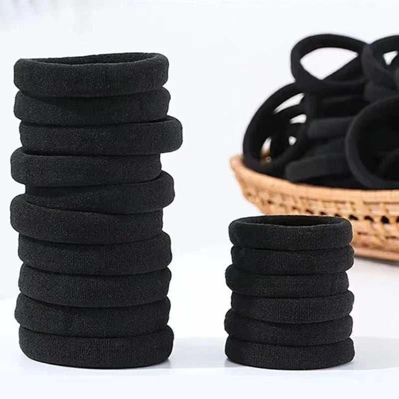 A stack of black elastic hair ties for ponytails and buns next to a basket of similar ties.