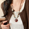A close-up of a bohemian heart beaded pendant necklace worn around the neck against a brown jacket and white top.