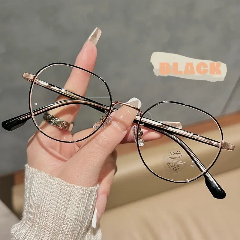 Une main tient une paire de lunettes fines à monture métallique et verres clairs sur un fond clair.
