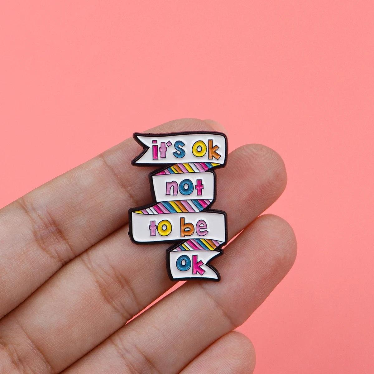 A hand holds a set of enamel pins with the text it's ok not to be ok and ok