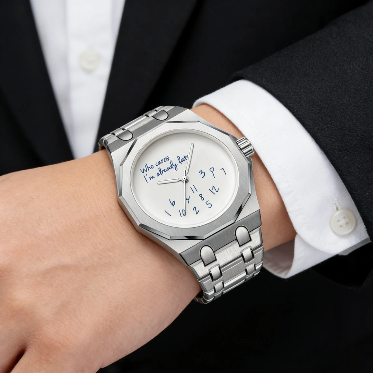 A close-up of a stainless steel watch with a light blue dial and a slogan on the face, worn on a wrist next to a black suit j