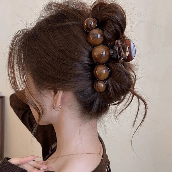 A close-up of a woman's dark brown hair styled in an elegant updo with a tortoiseshell acrylic pearl hair claw clip.