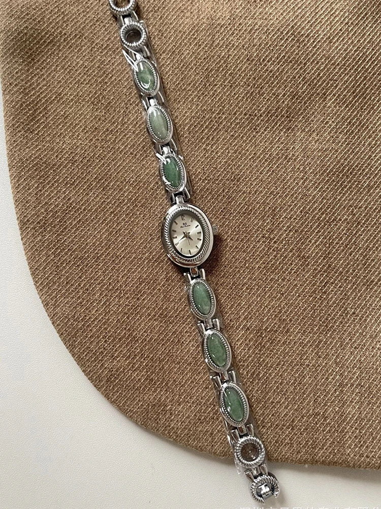 Montre en quartz jade verte élégante avec des maillons argentés et un cadran rond sur fond de tissu brun.