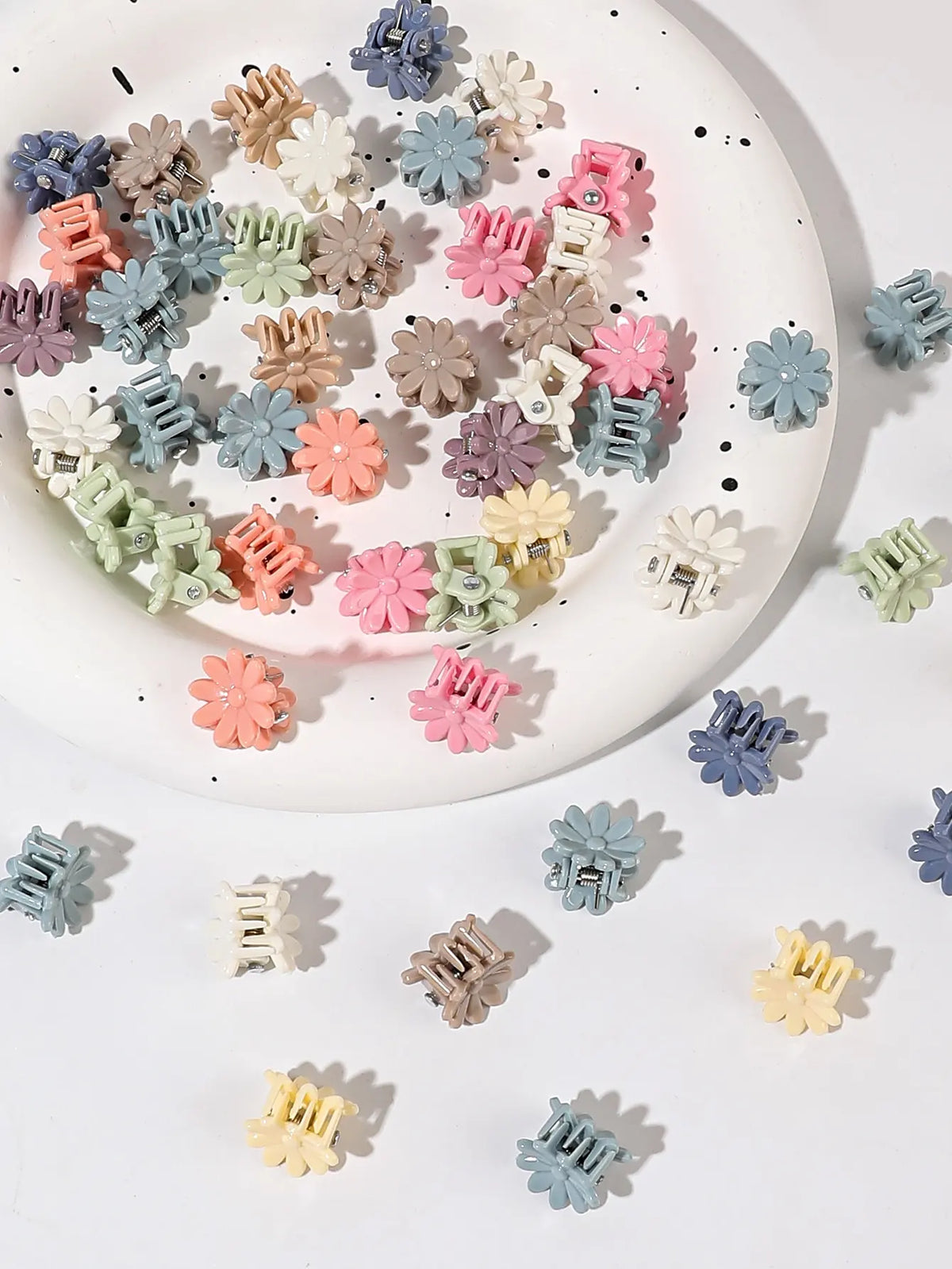 A collection of colorful mini flower hair clips in various shades of pink, purple, green, and beige scattered on a white plat