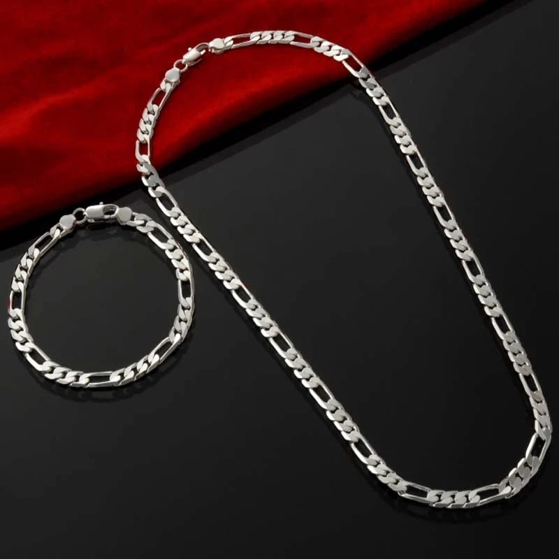 A silver charm necklace and bracelet set displayed on a dark surface with a red fabric background.