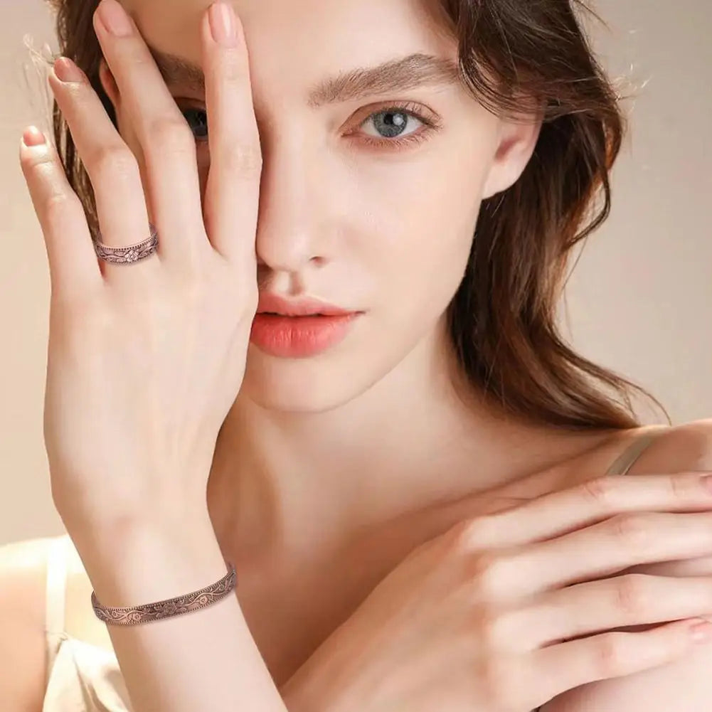 A close-up of a woman's hand wearing a vintage flower engraved copper bracelet and ring set.