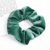 A close-up shot of a dark emerald green velvet scrunchie, showing its textured fabric and gathered design.
