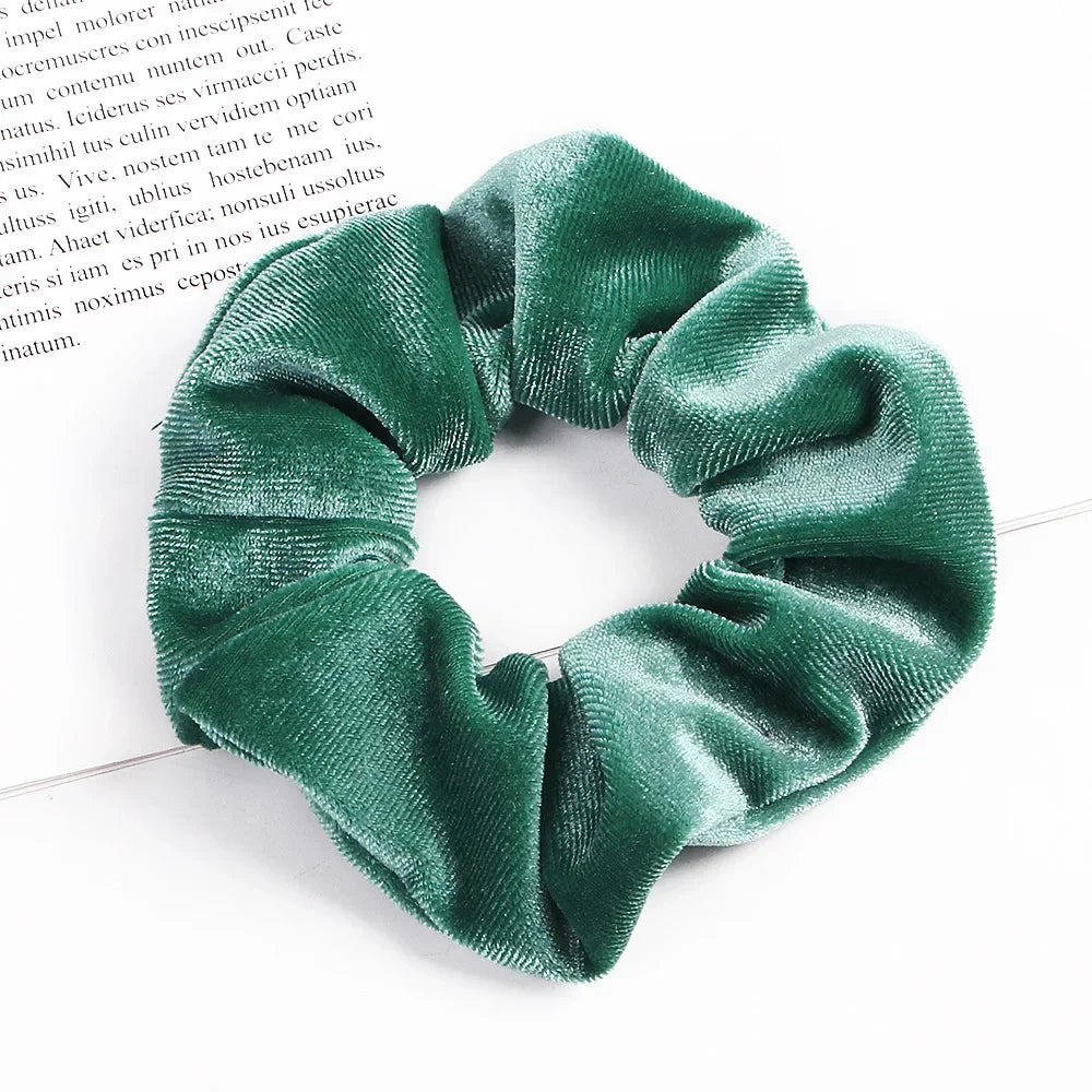 A close-up shot of a dark emerald green velvet scrunchie, showing its textured fabric and gathered design.