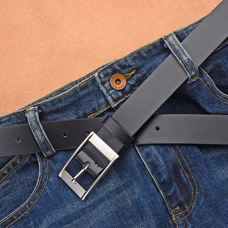 A close-up of a dark gray PU leather belt with a silver metal pin buckle worn on blue denim jeans.