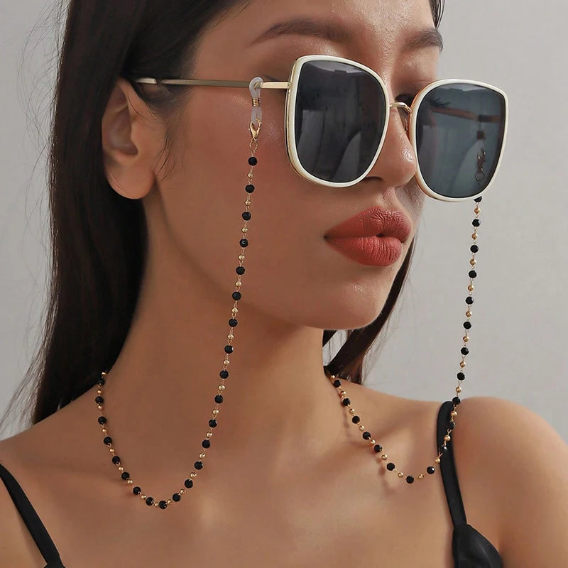 A close-up of a woman wearing stylish sunglasses with gold frames and black bead lanyards around her neck.