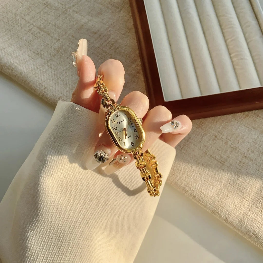 A hand holds a gold-toned quartz fashion wristwatch against a light beige fabric background.