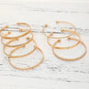 A set of elegant gold hexagon star twist bangles displayed on a white wooden surface.