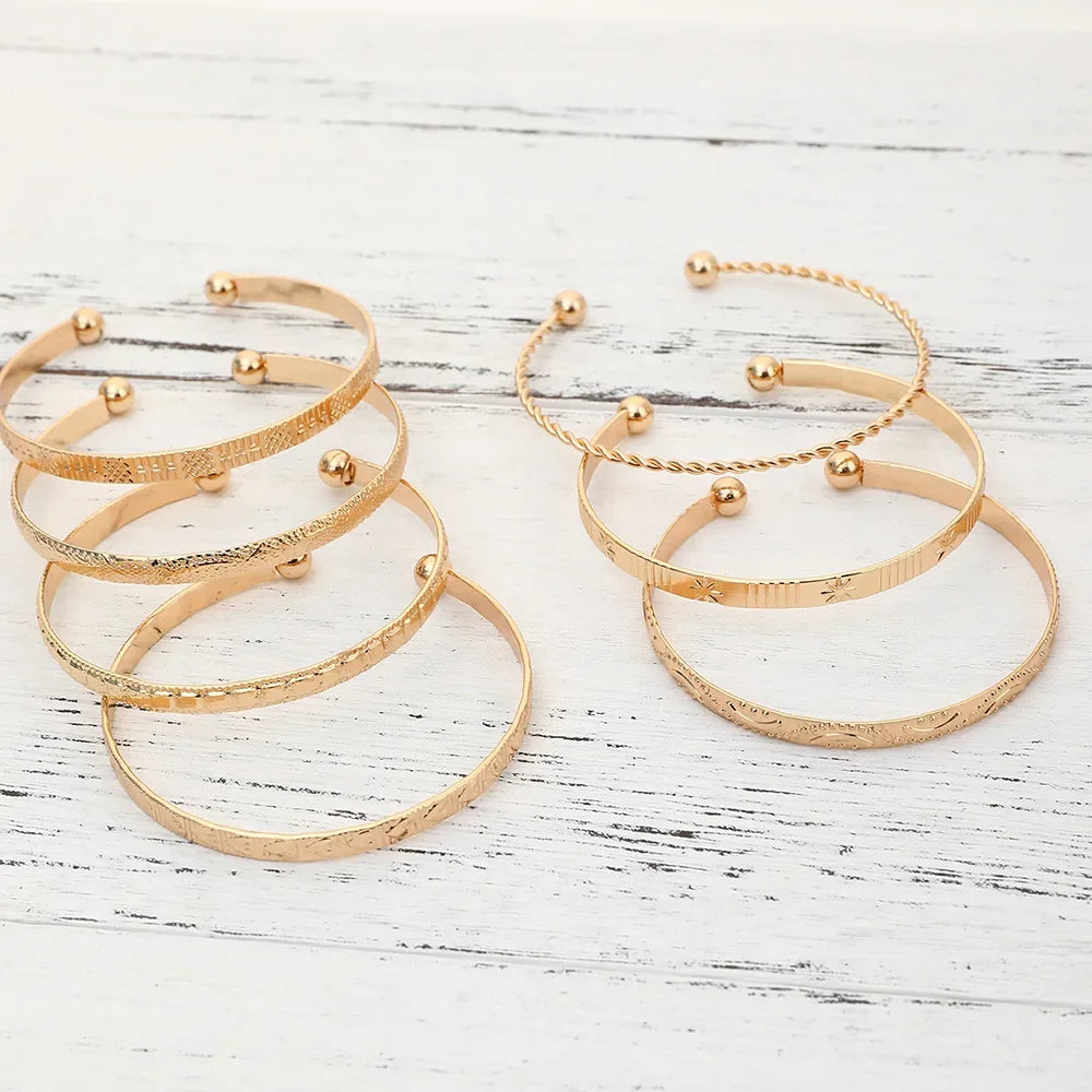 A set of elegant gold hexagon star twist bangles displayed on a white wooden surface.