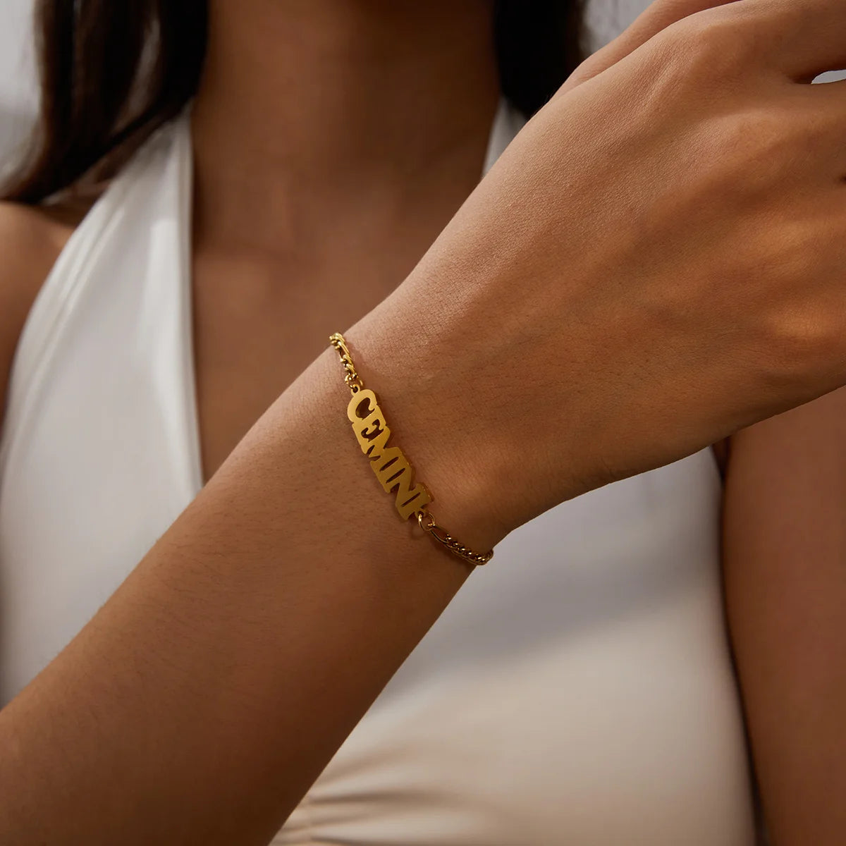 A close-up of a hand wearing a gold stainless steel charm bracelet with the zodiac constellation Cemis.