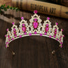 A sparkling gold crystal rhinestone tiara and headband set with pink gemstones resting on a dark wooden surface.