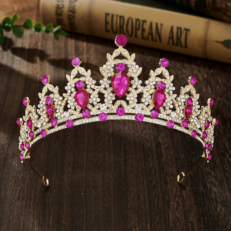 A sparkling gold crystal rhinestone tiara and headband set with pink gemstones resting on a dark wooden surface.