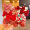 A hand holds a display of red and white checkered and solid red flower bow hair ties for girls.