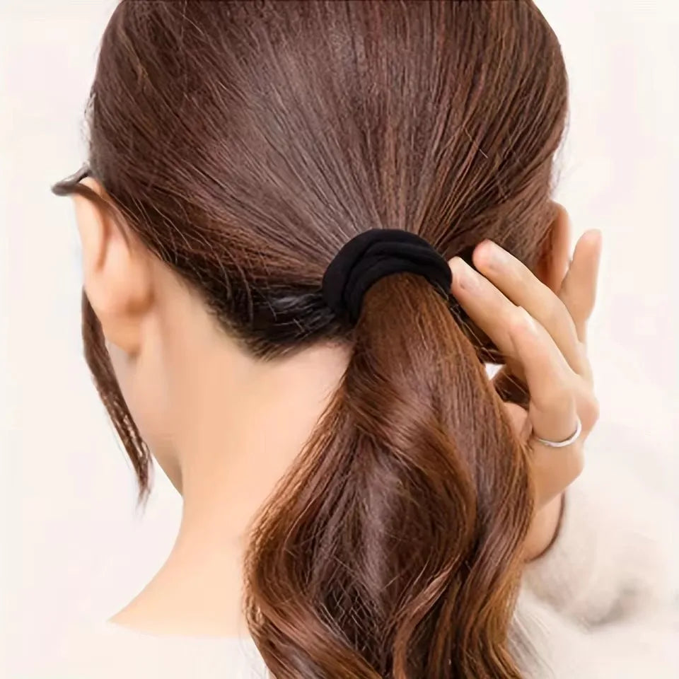 A hand is tying a ponytail with a black elastic hair tie on a woman's brown hair.