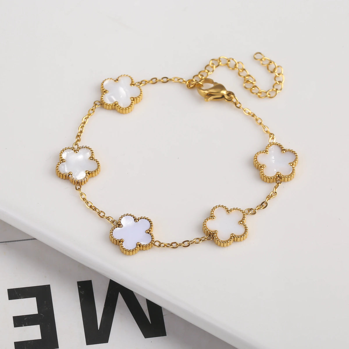 Pulsera de acero inoxidable chapada en oro con pequeños charms de flores blancas en una cadena dorada.
