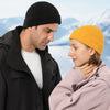 A man and a woman looking at each other outdoors, one wearing a black coat and the other an orange knitted beanie.