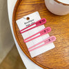 A set of five pink vintage frosted geometry hair clips packaged on a white card resting on a wooden tray.