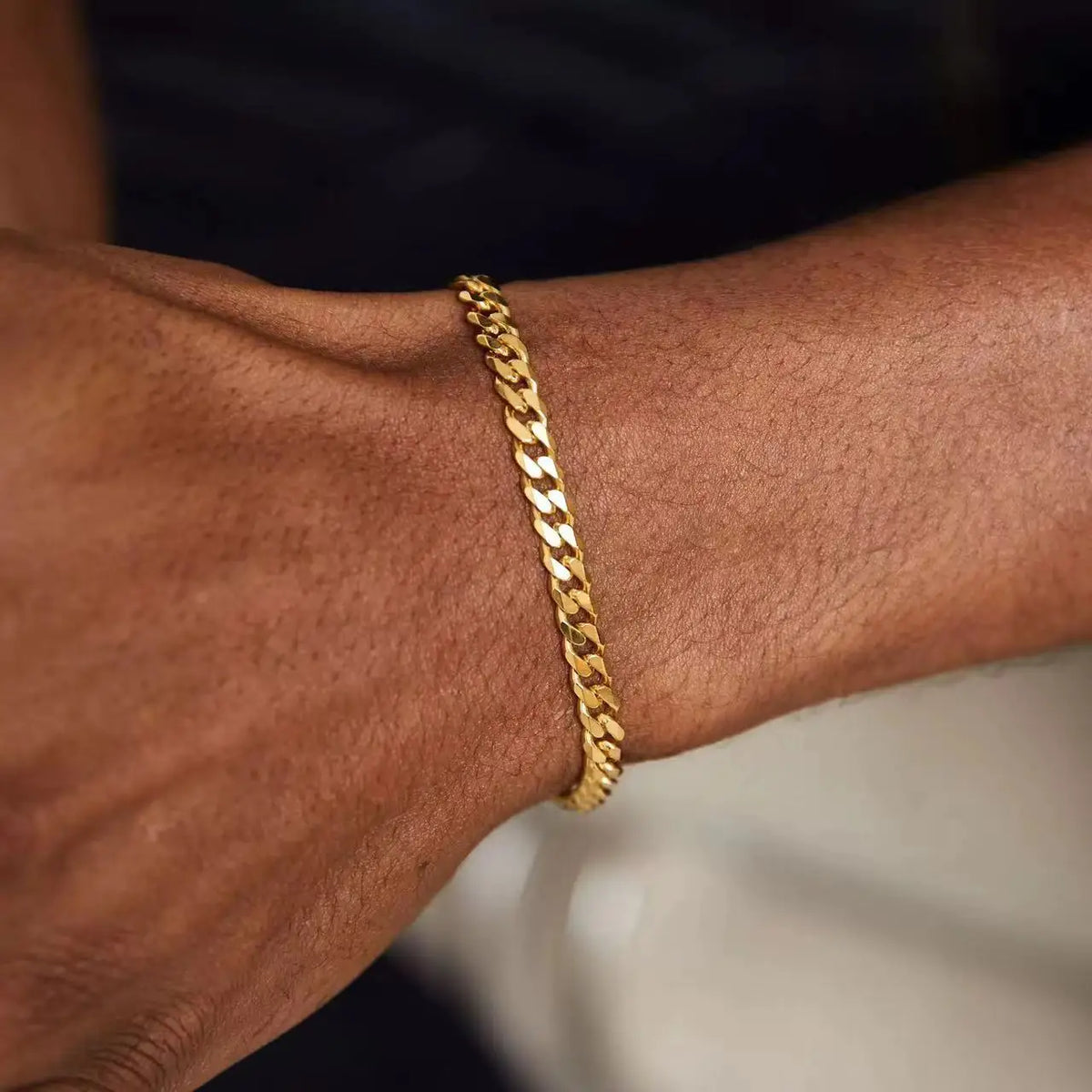 A close-up of a gold-toned stainless steel Cuban link bracelet worn on a person's wrist.