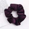 A close-up shot of a dark purple velvet scrunchie resting on a white background.