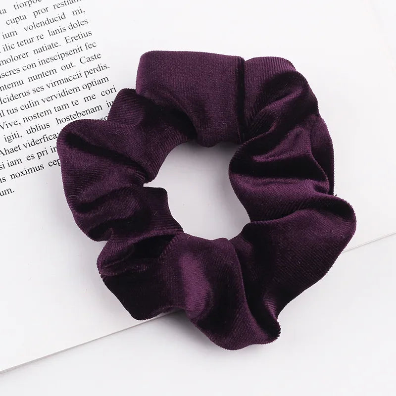 A close-up shot of a dark purple velvet scrunchie resting on a white background.