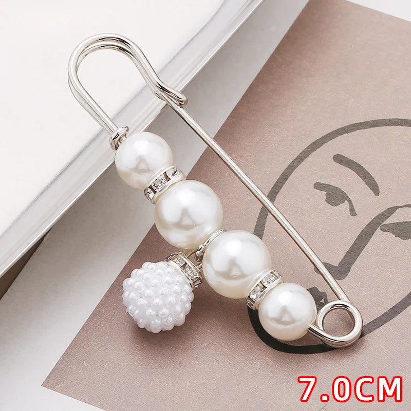 A silver safety pin decorated with multiple white pearls and clear stones, shown on a brown card.