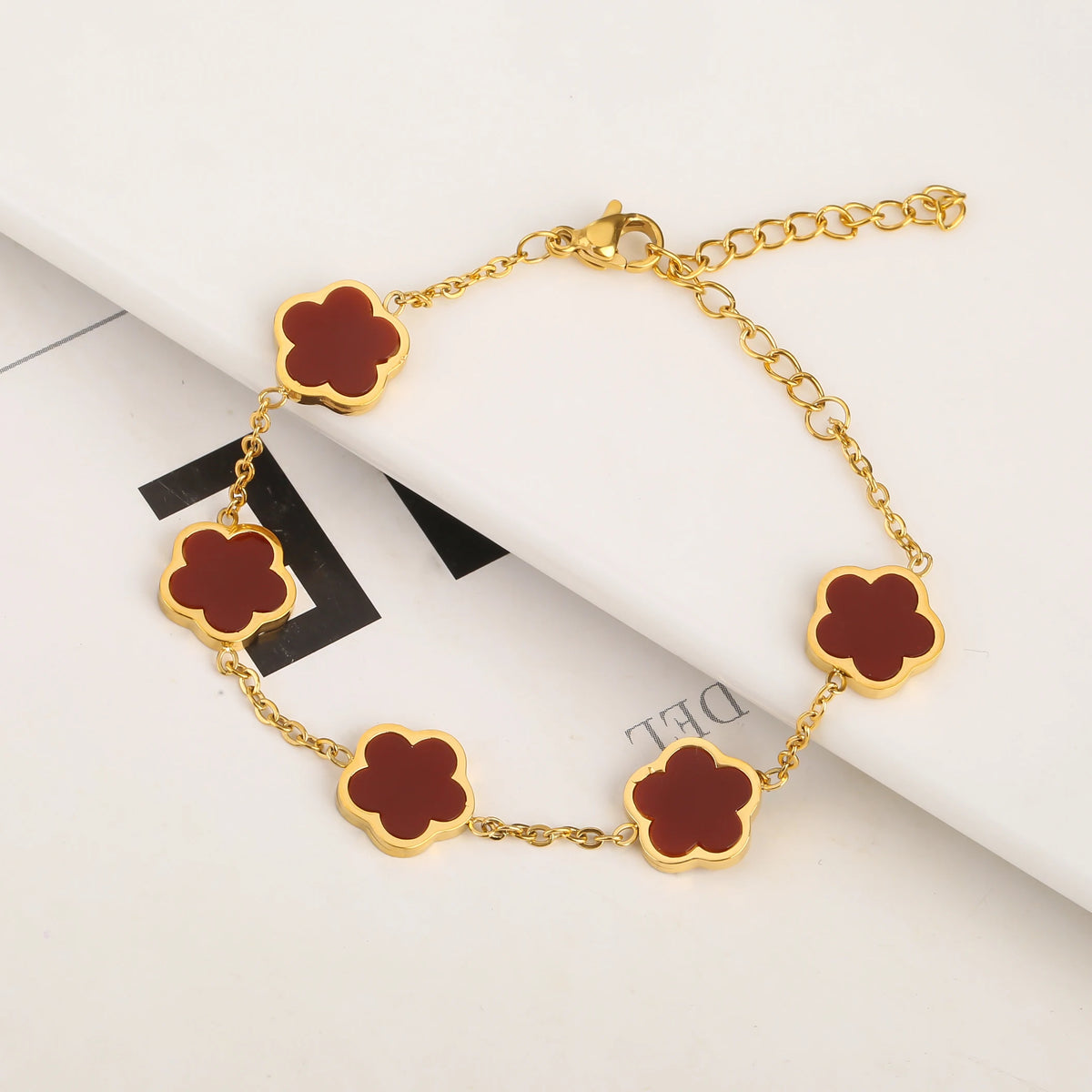 Pulsera de acero inoxidable chapado en oro con pequeños colgantes en forma de flor y esmalte marrón rojizo.