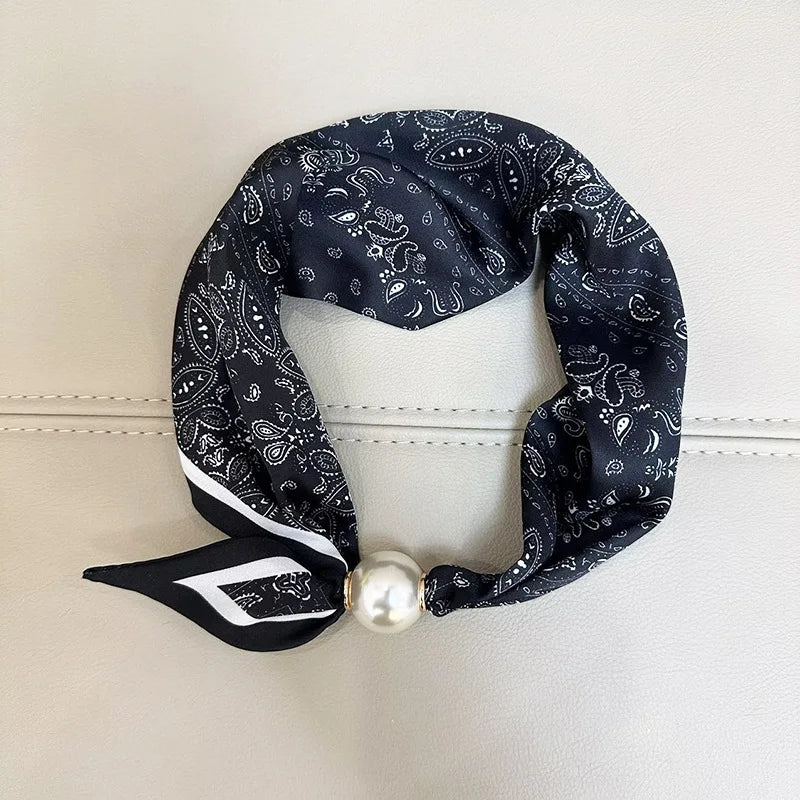 A black patterned scarf with white trim and a pearl tail magnetic clasp displayed against a light background.