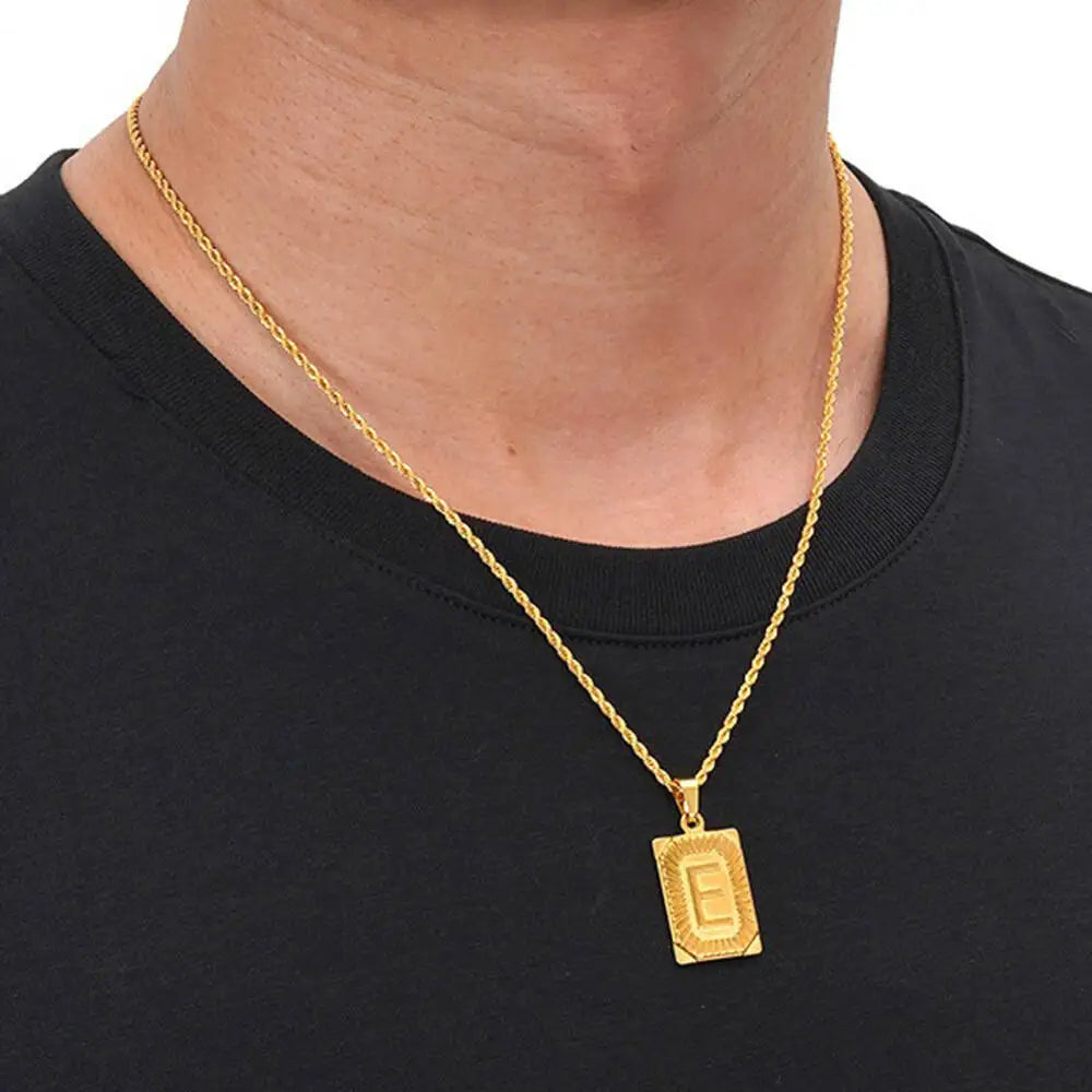 A gold-plated letter pendant necklace with a thin chain worn around the neck against a black shirt.
