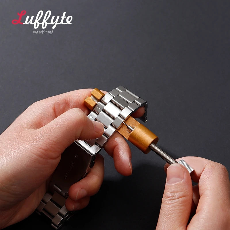 A hand is using a watchband repair tool to adjust or fix a metal bracelet or watch strap.