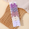 A collection of purple and pink handmade ribbon bow hair clips displayed on a white card against a wooden background.