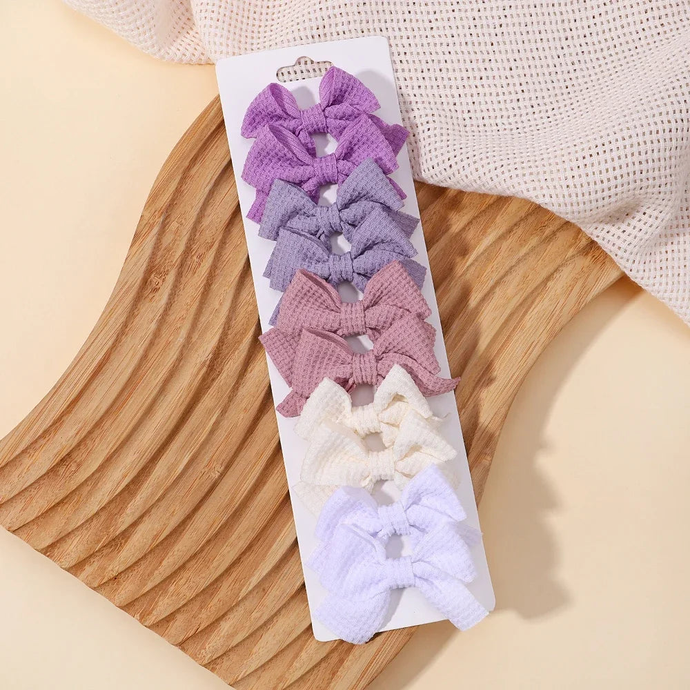 A collection of purple and pink handmade ribbon bow hair clips displayed on a white card against a wooden background.