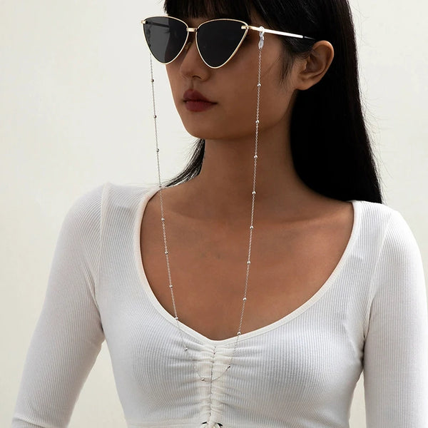A woman wearing round metal beads sunglasses with a long chain necklace and a white top.