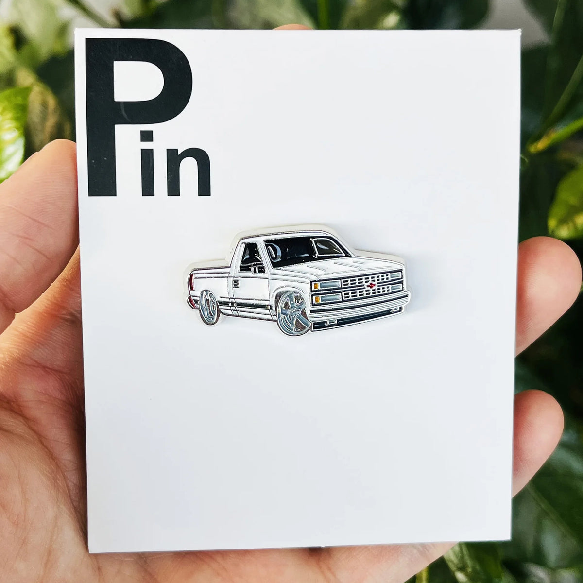 A silver and white pickup truck metal clip pin is displayed on a white card.