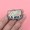 Una mano sostiene un pin de esmalte inspirador con el texto: 'Puedes hacer cosas difíciles'.