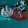 A sparkling rhinestone bridal hair hoop is displayed next to a clear crystal crown on a teal velvet background.