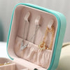 A light pink and mint green compact leather jewelry travel organizer box displaying silver and gold necklaces.