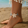 A woman wearing a white and orange flower anklet on her ankle while standing on the beach.
