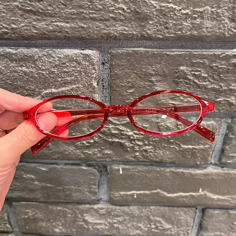 Une main tient une paire de lunettes de mode ovales rouges contre un mur de briques grises.