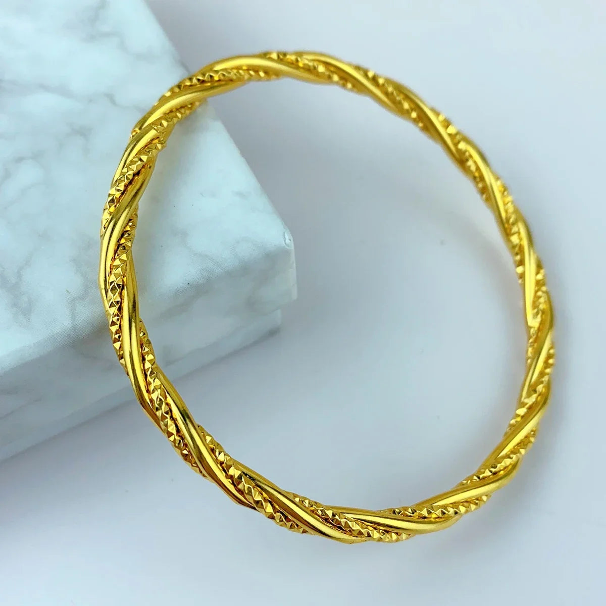Nahaufnahme eines dünnen, goldfarbenen geometrischen Armbandes auf einer weißen Marmoroberfläche.