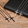 Tres collares de cruz de acero inoxidable exhibidos en una caja negra contra un fondo de madera.