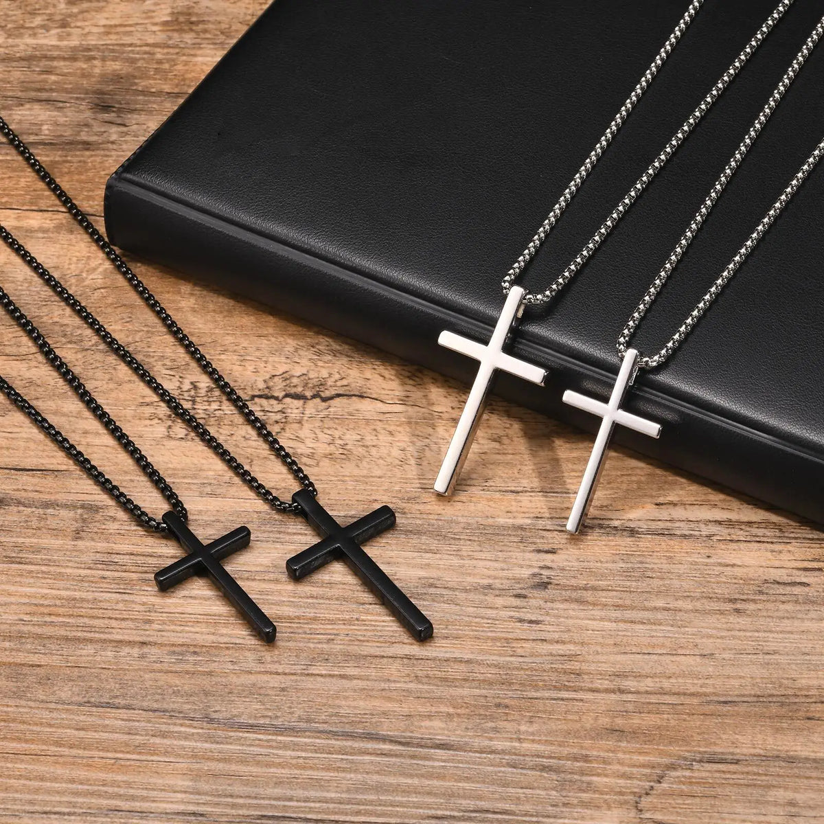 Tres collares de cruz de acero inoxidable exhibidos en una caja negra contra un fondo de madera.